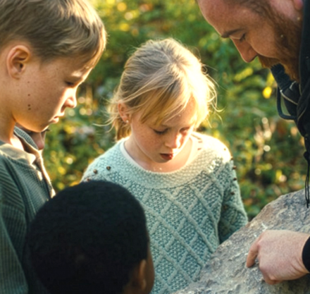 a man and children looking at a rock